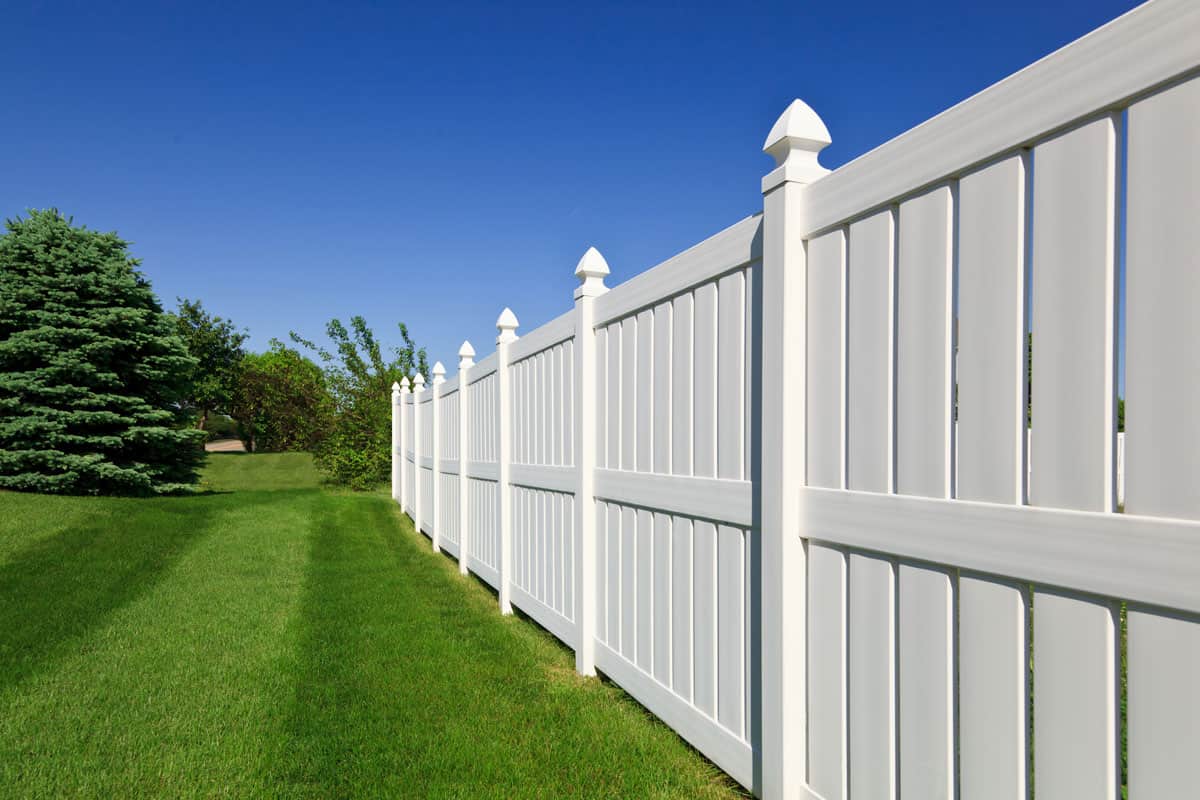 white vinyl fence running across a nicely landscaped backyard