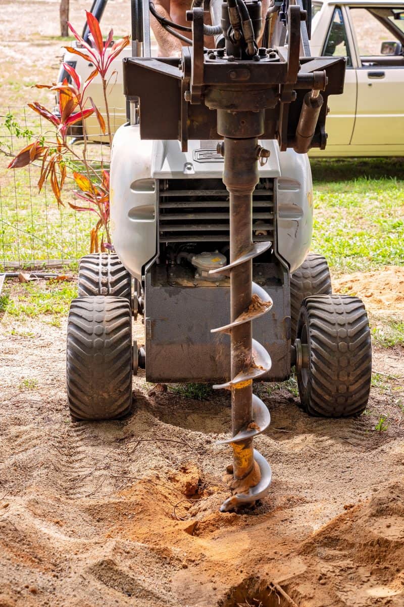A machine with auger attached for digging post holes in the soil
