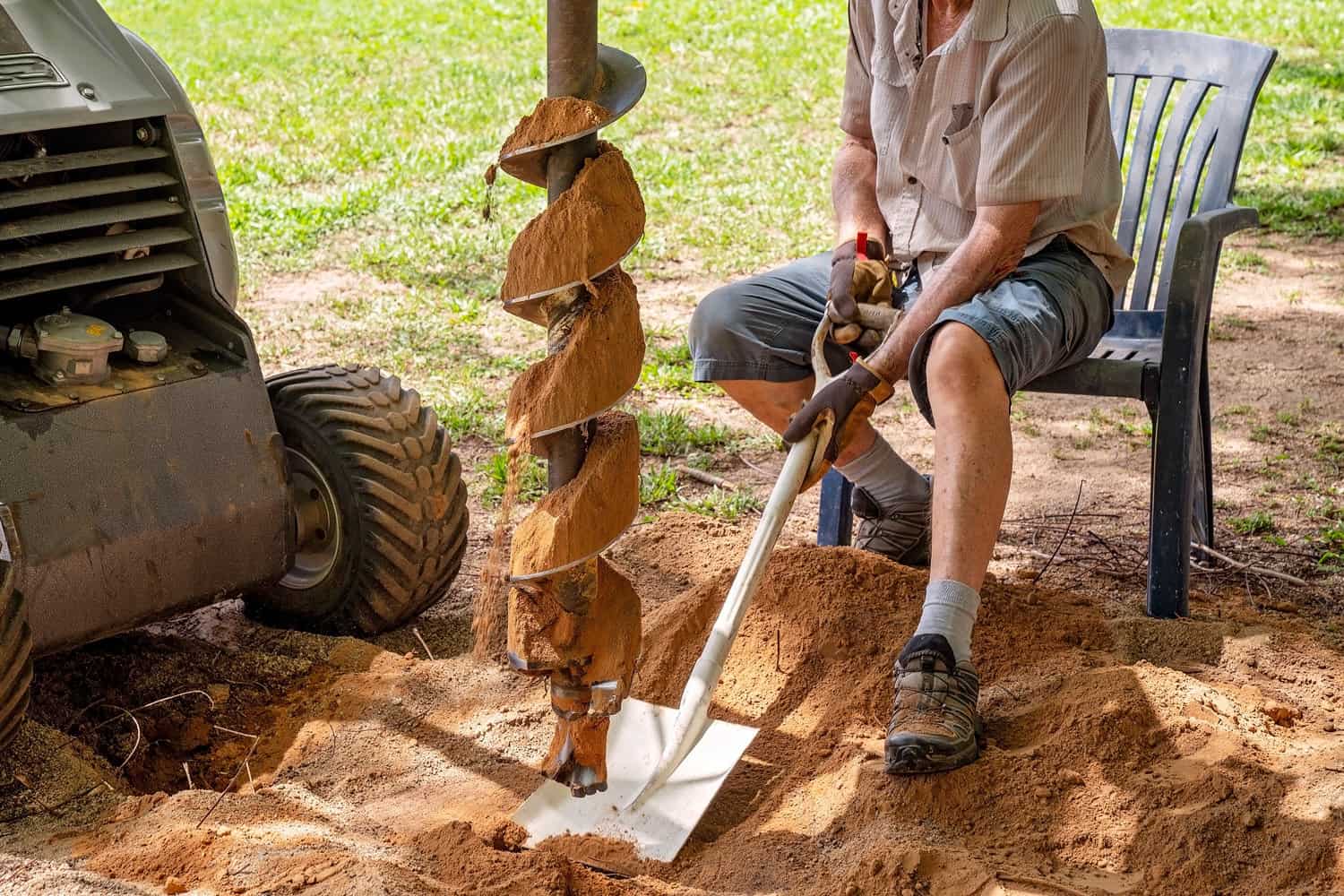 A mechanical auger digging holes in the soil with the aid of a senior male with a shovel