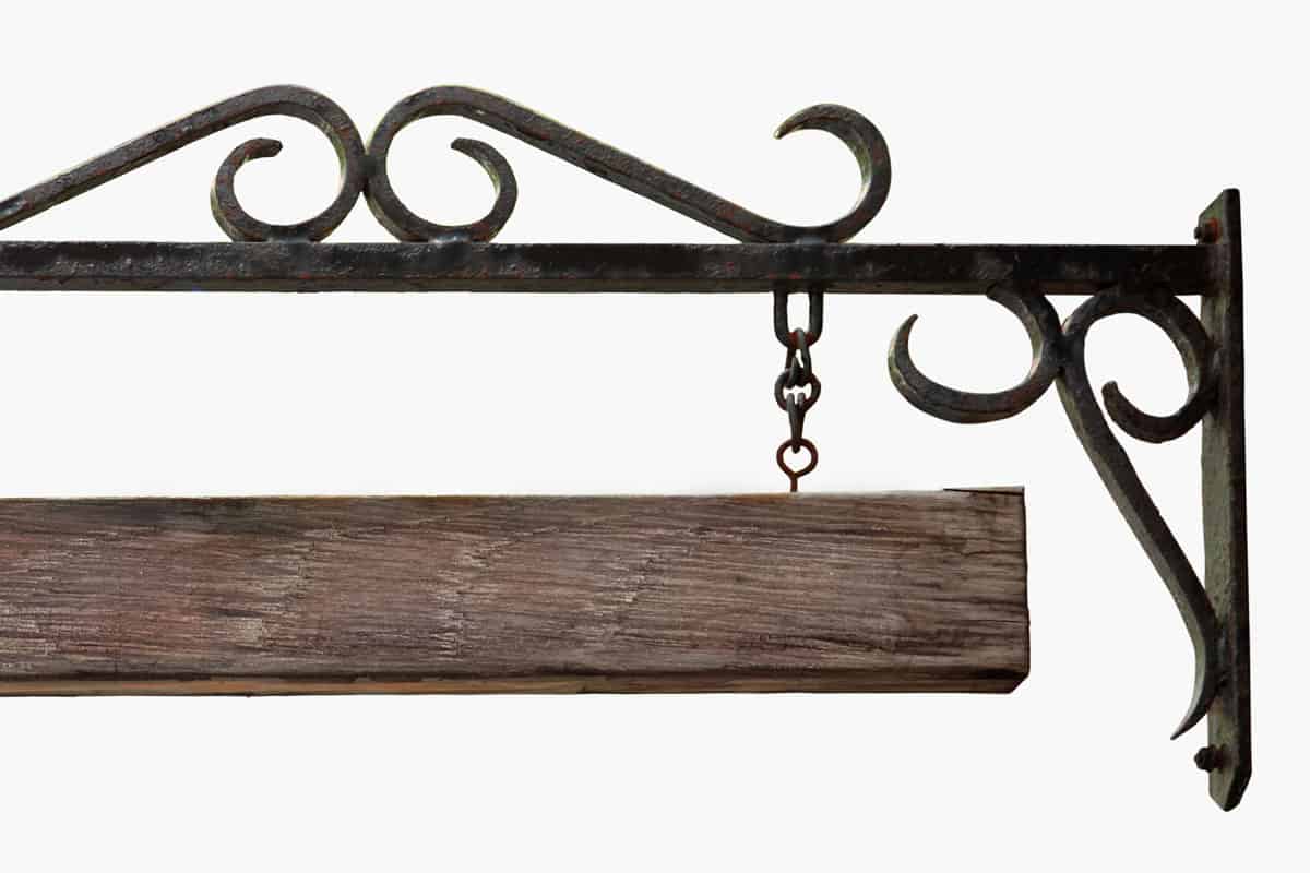An old black hanging sign made from wrought iron with a blank wooden board hanging from chains