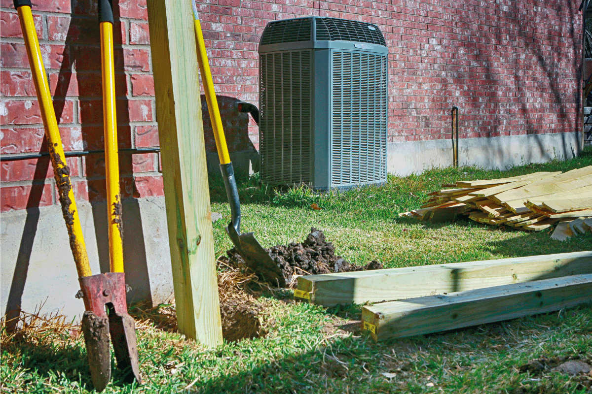 Backyard with modern air conditioner, shovels and lumber for new privacy fence. How To Use a Post Hole Digger In Hard Ground