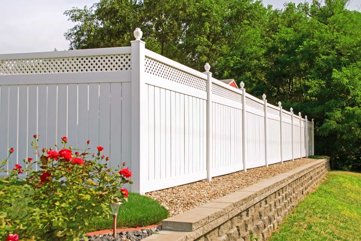 Beautiful white vinyl fence in back yard with nice landscaping in the foreground and background

