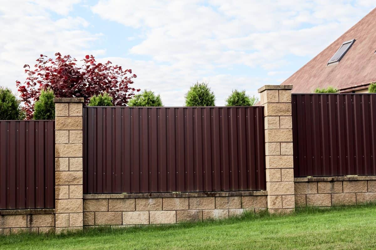 Brown metal profile fence with block posts. Incline construction. Corrugated surface.