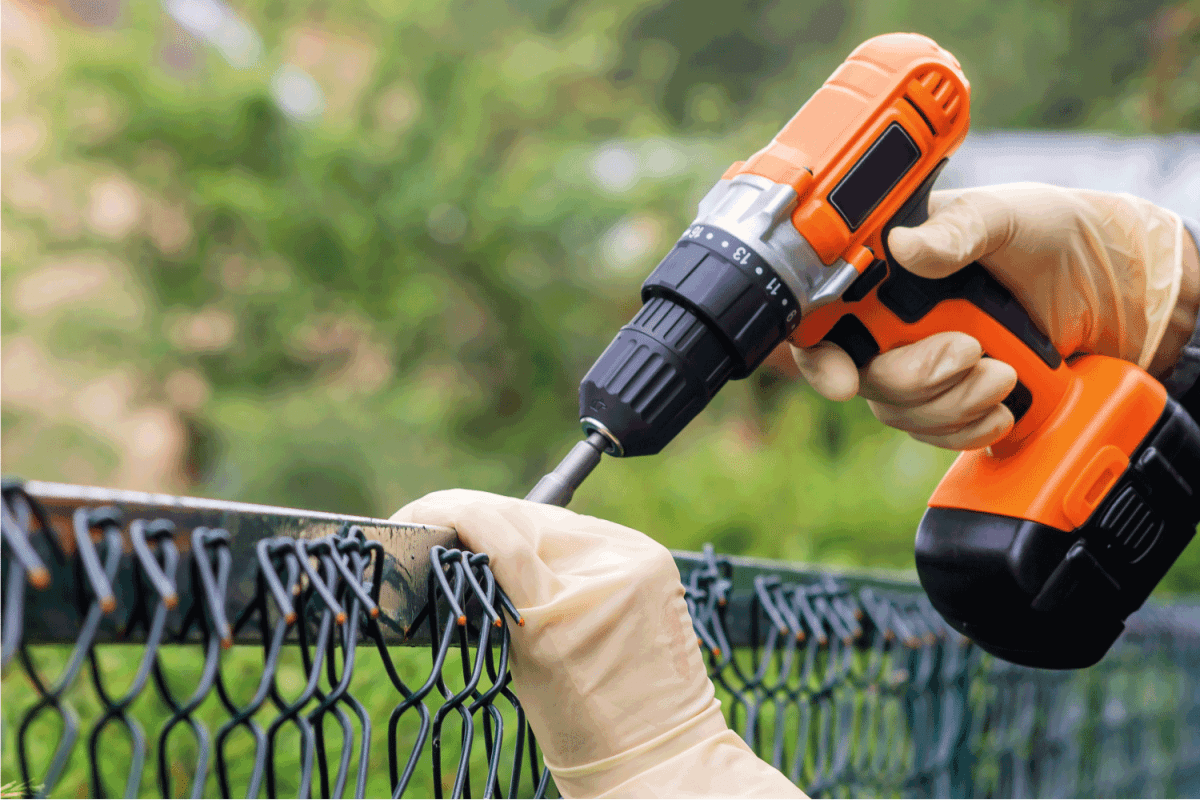 Fastening the metal mesh of the chain-link with a drill-screwdriver with an electric battery on the fence.
