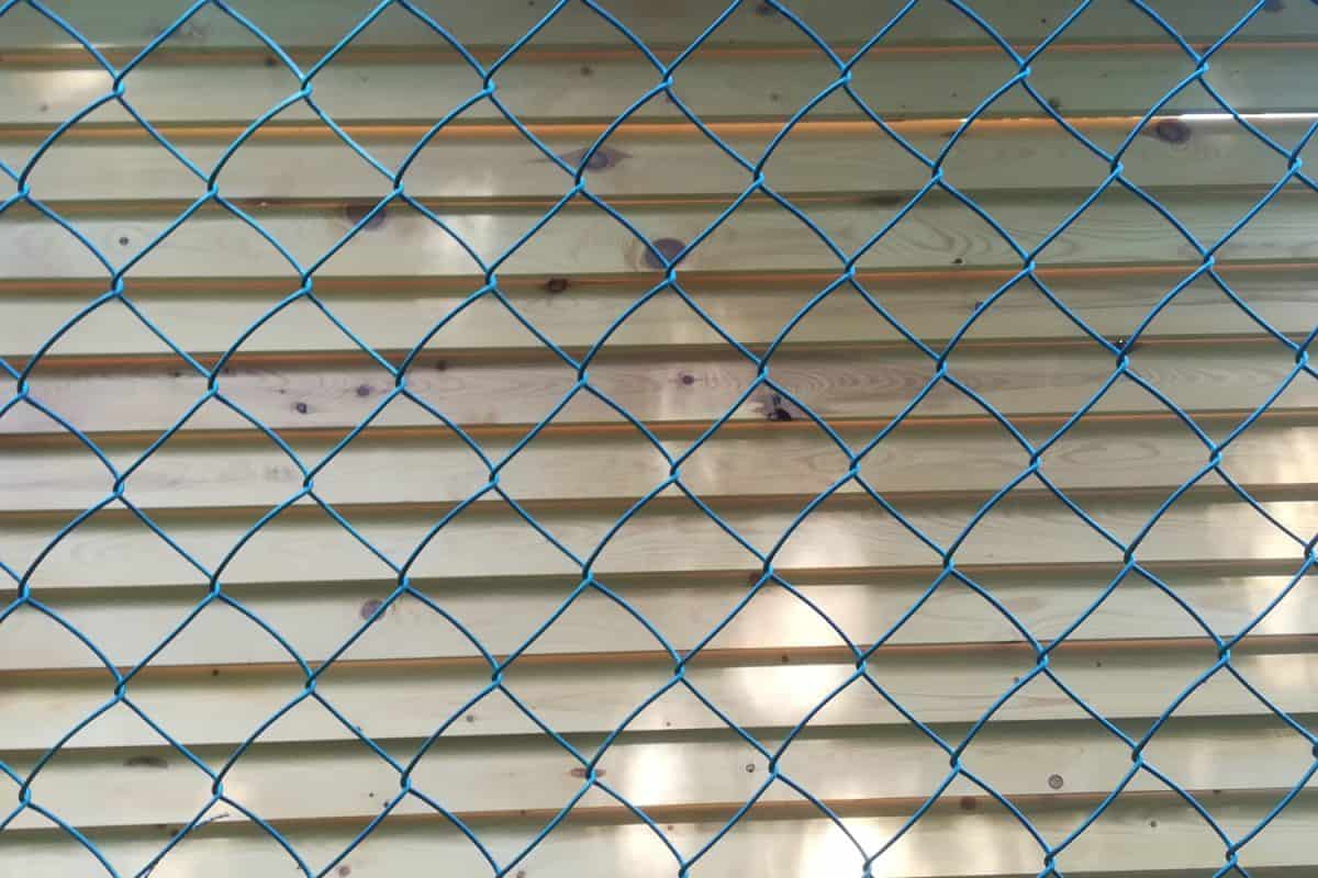 Metal mesh chain-link on a background of a wall made of wooden boards.
