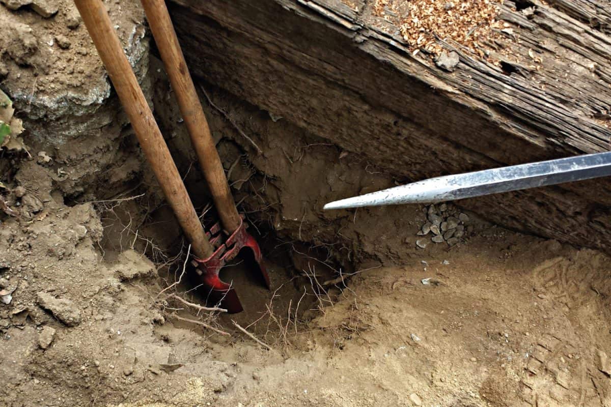 Proper tools such as a posthole digger and a rock bar are being used to dig a fence post hole.