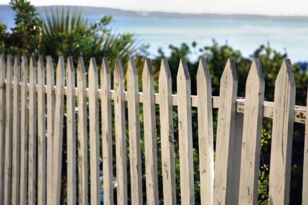 White wooden picket fence with water, foliage and coastline showing in the distance