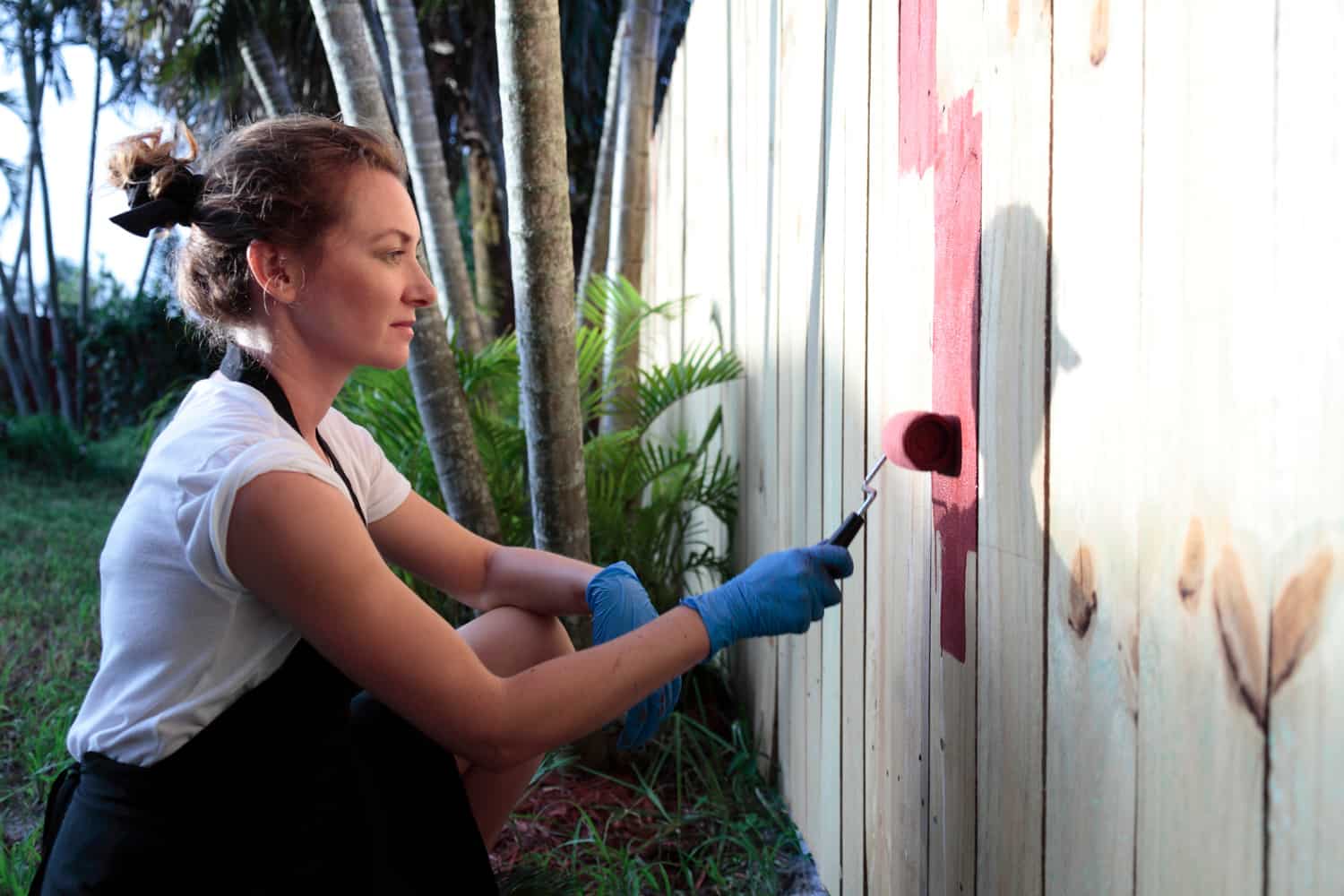 Young woman is painting a fence