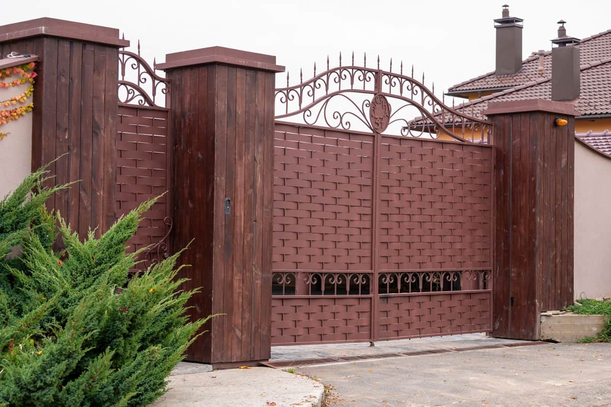 forged metal fence on stone pillars sheathed with wood panels in front of the house