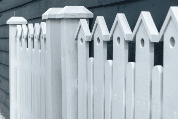 white fence with small decorative birdhouse with a hole on the top of each paling.