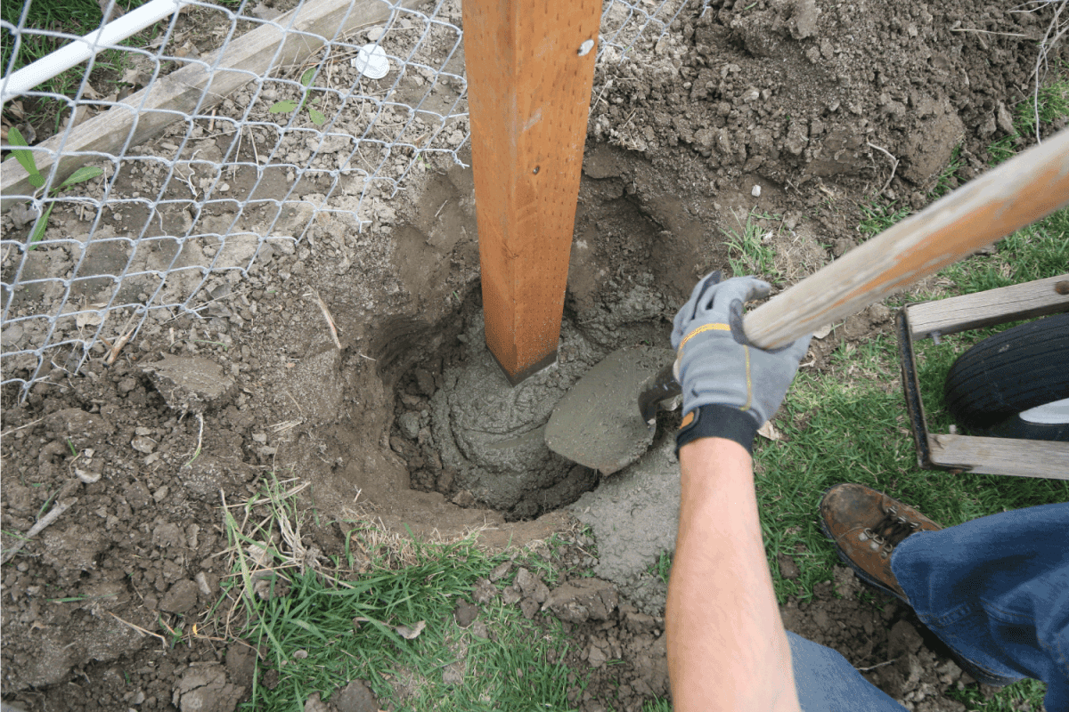 worker shoveling concrete mixture into the fence post footing