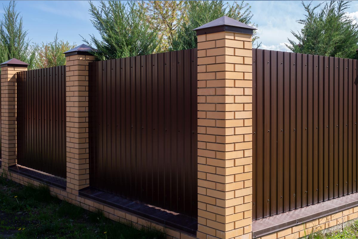 A brown metal fence with brick posts against a sky