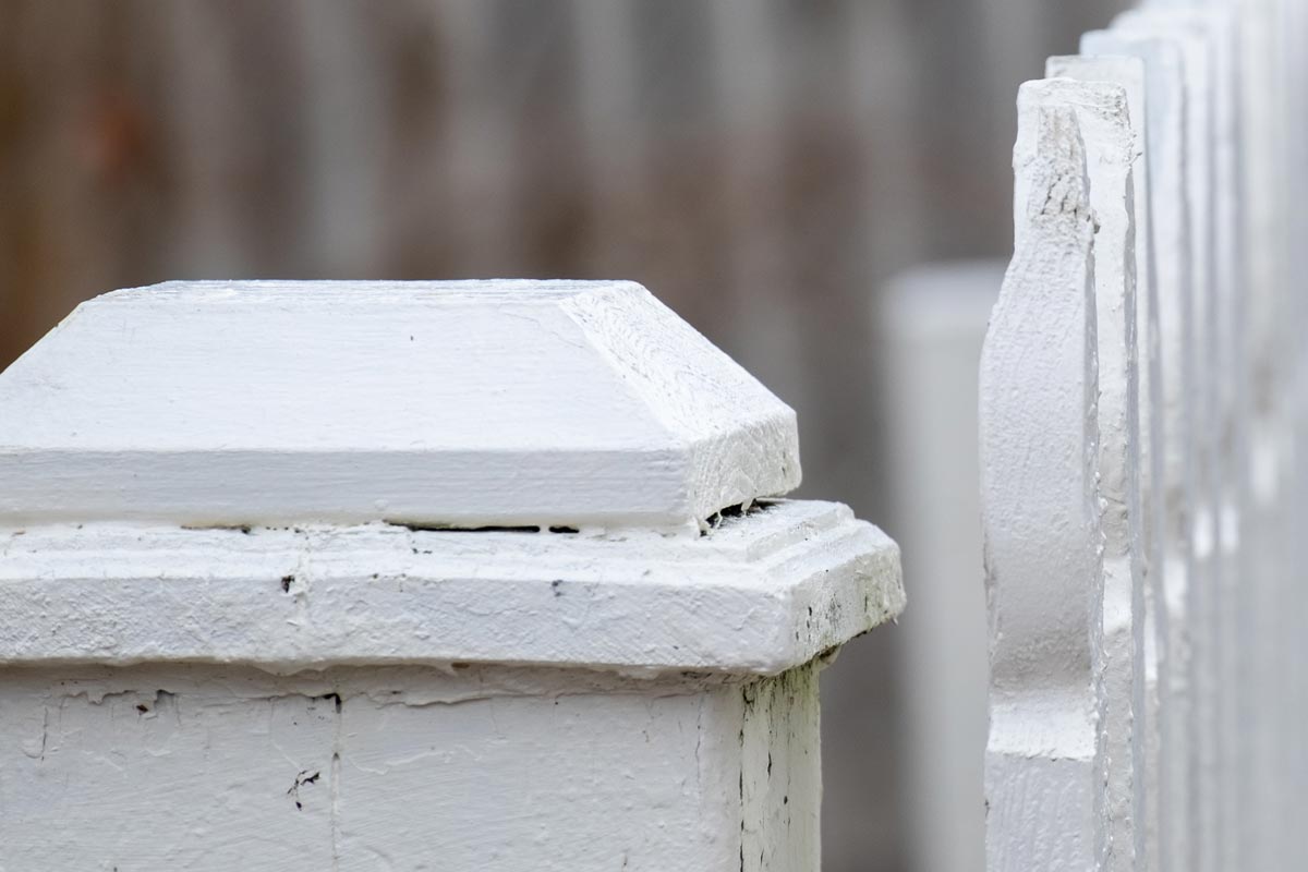 A close up of an antique white wooden picket fence post with vertical wooden pailings having a curved shape on top