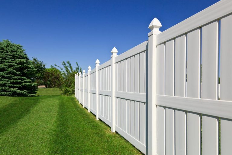 A new white vinyl fence running across a nicely landscaped backyard, Do Vinyl Fences Reduce Noise?