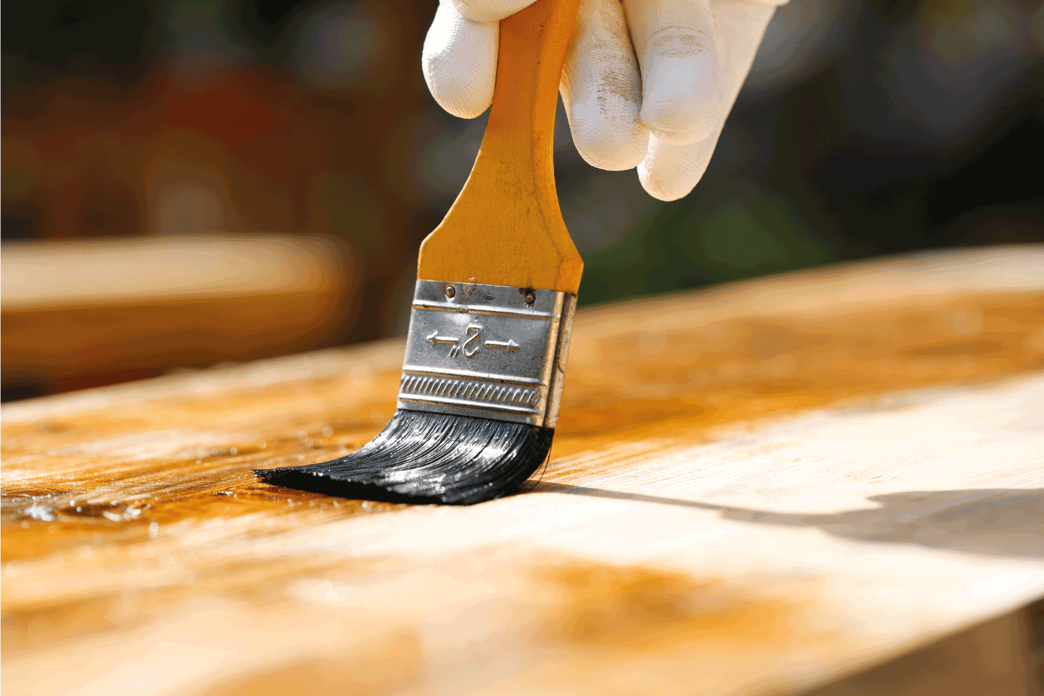 Painter holding a paintbrush over wooden surface, protecting wood for exterior influences and weathering.