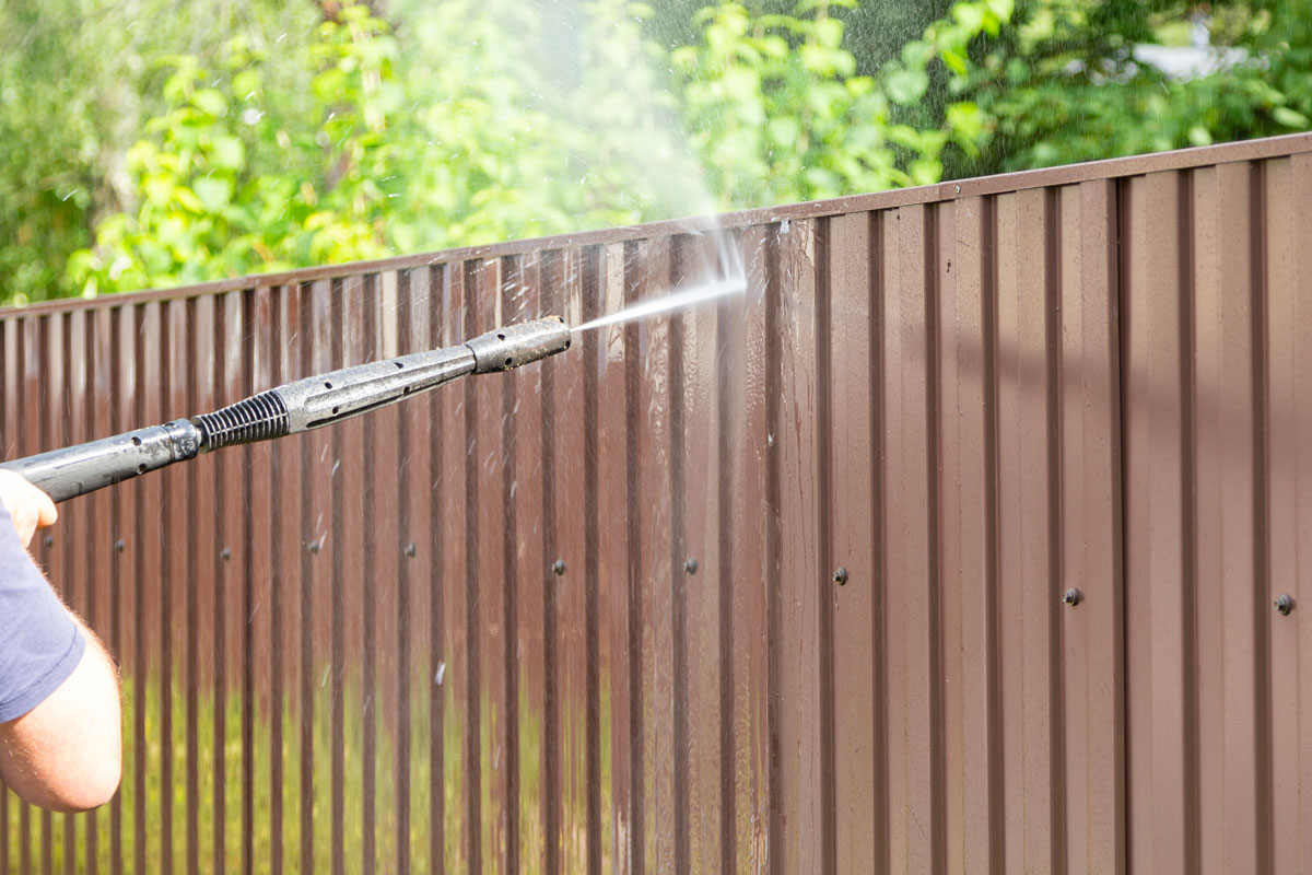 Power spray cleaning the brown colored fence