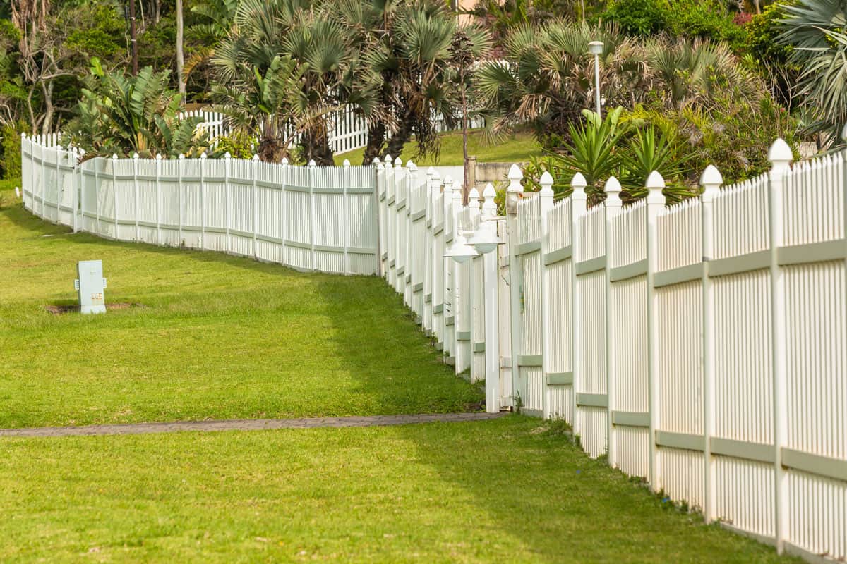 White boundary vertical slat plastic pvc fence wall along roadside grass landscape