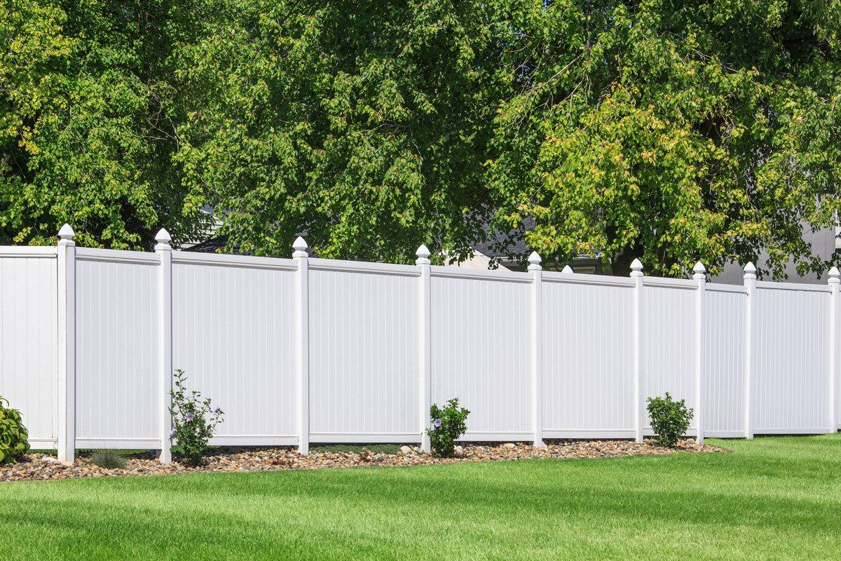 White vinyl fence running across a homeowners back yard.

