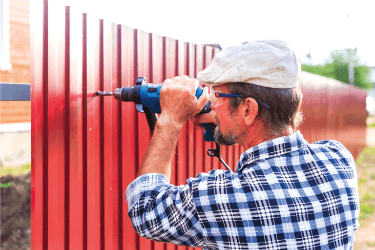 an elderly man with a drill builds metal fence. Are T Posts Galvanized [Do They Rust]